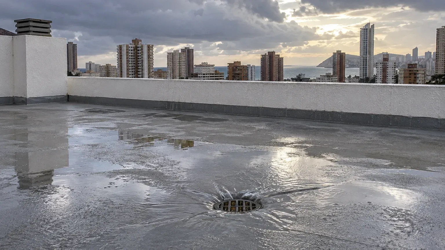 Azotea de un edificio de Benidorm con charcos tras una tormenta de otoño y el sumidero evacuando agua